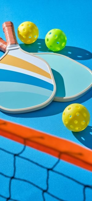 pickleball paddles with balls to the side on a blue background illuminated with hard light