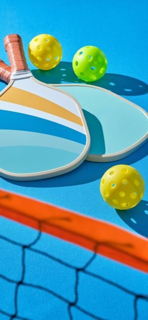 pickleball paddles with balls to the side on a blue background illuminated with hard light